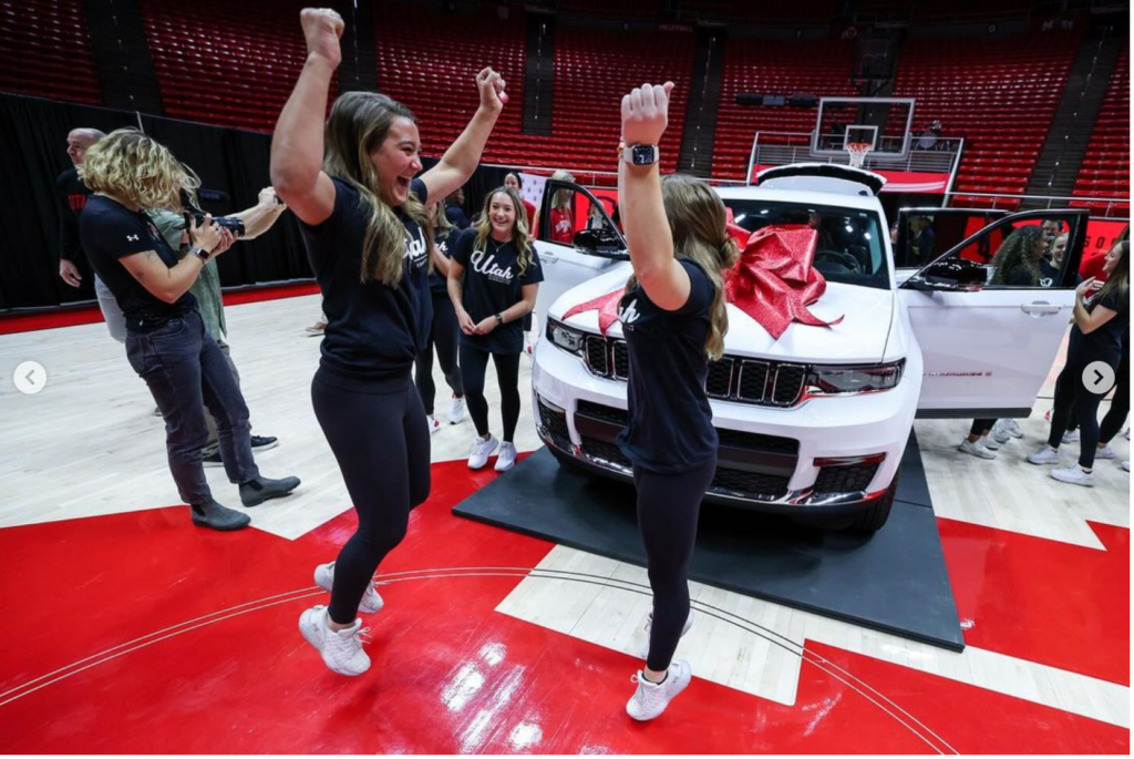 Utah athletes celebrate around a white vehicle with a red bow on it.